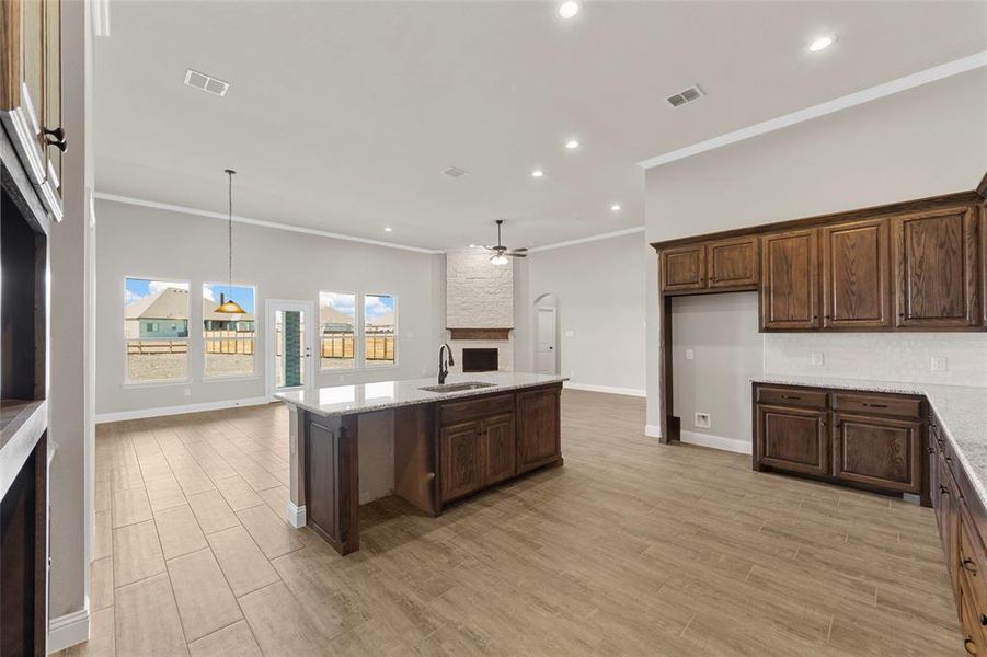 Kitchen featuring a stone fireplace, decorative light fixtures, sink, and light stone counters