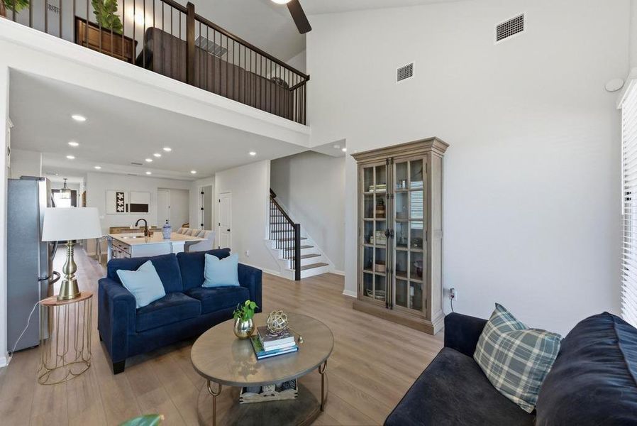 Living area featuring light wood-type flooring, stairway, a towering ceiling, and recessed lighting
