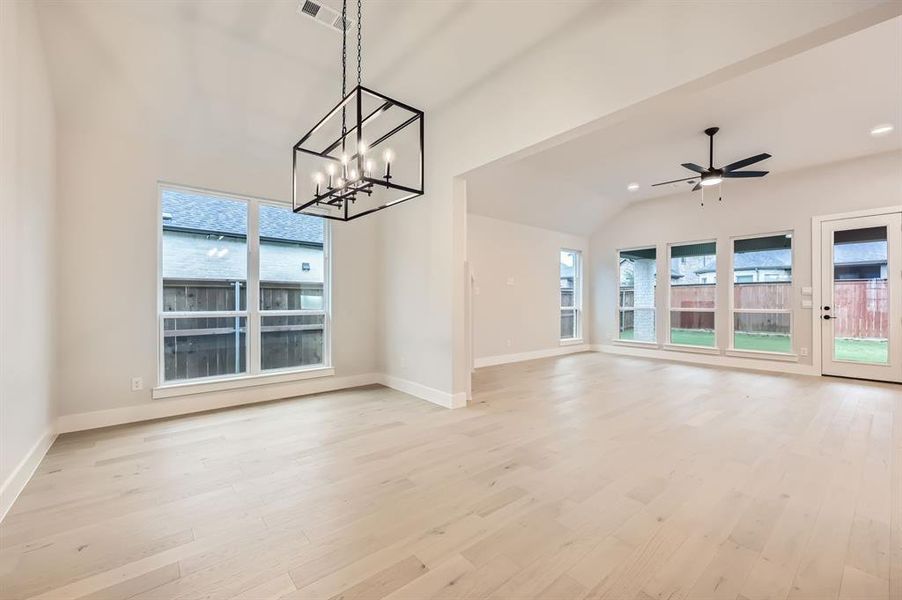 Unfurnished living room featuring ceiling fan with notable chandelier, light hardwood / wood-style floors, and lofted ceiling