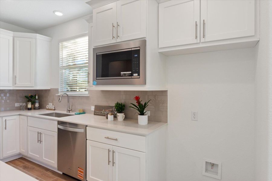 Kitchen with white cabinetry, stainless steel appliances, backsplash, lower cabinets have roll-out drawers
