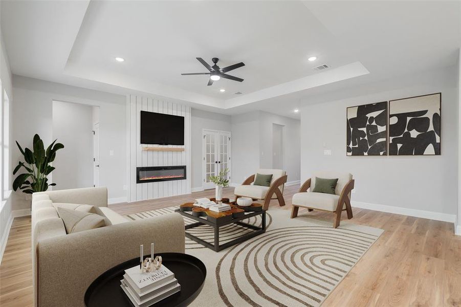 Living room with light wood-type flooring, ceiling fan, and a raised ceiling