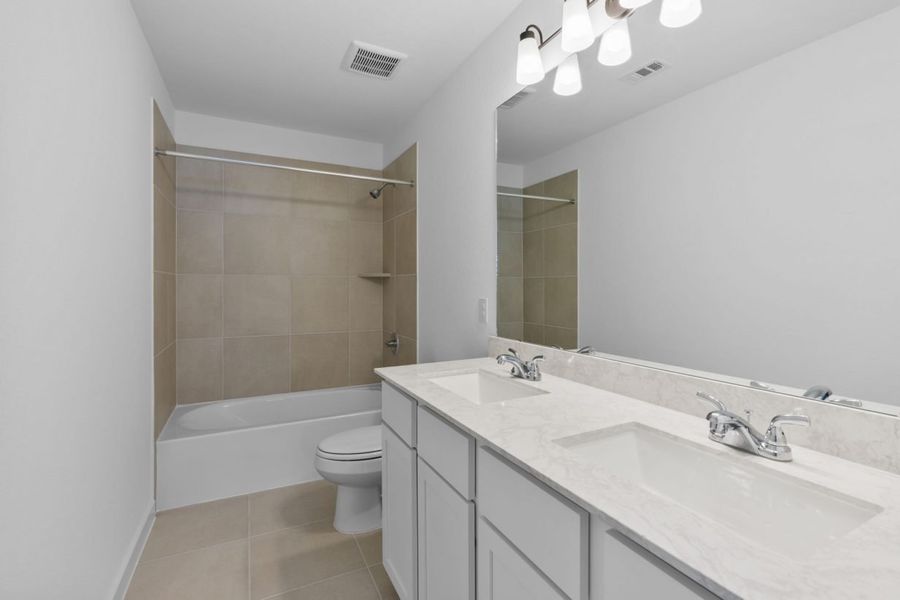 Image of a secondary bathroom with a jack and jill vanity, a large mirror, and a a shower and tub with tan tiles Image of a secondary bathroom with a jack and jill vanity, a large mirror, and a a shower and tub with tan tiles