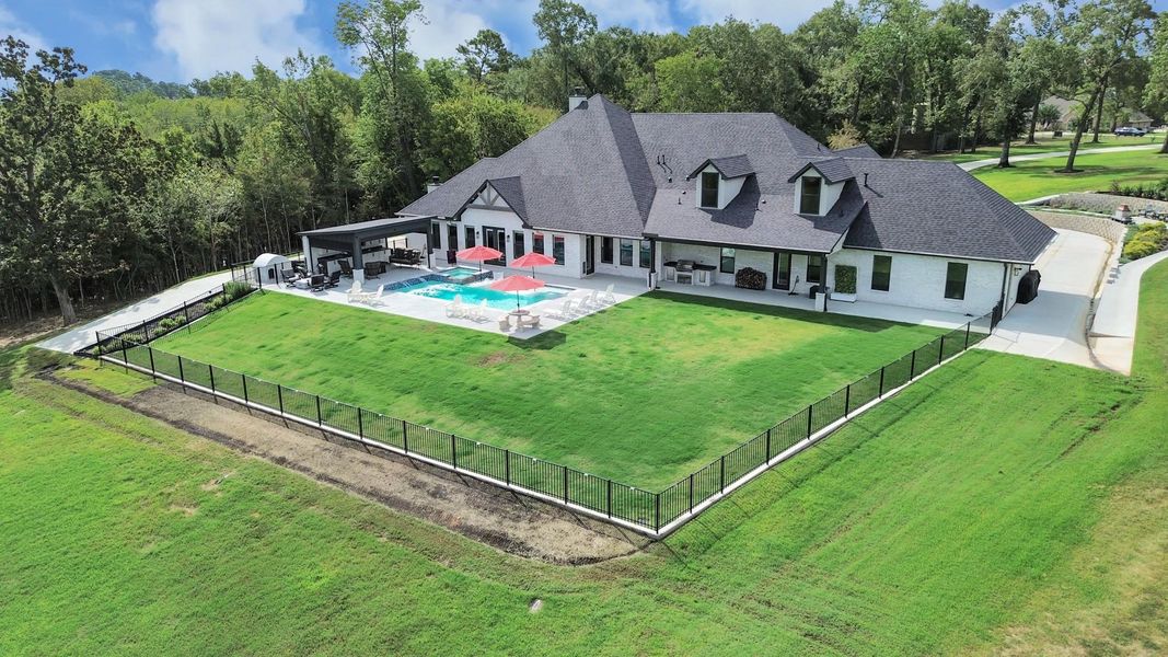 Stunning estate featuring a spacious backyard with a sparkling pool and covered patio, surrounded by lush greenery and a secure fence for privacy.