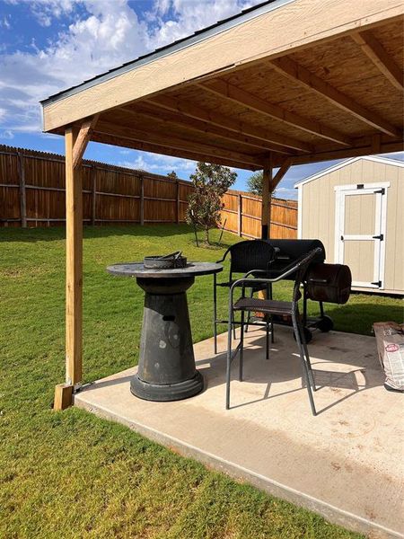 Fenced backyard featuring a patio area, a storage unit, and a fire pit Fenced backyard featuring a patio area, a storage unit, and a fire pit
