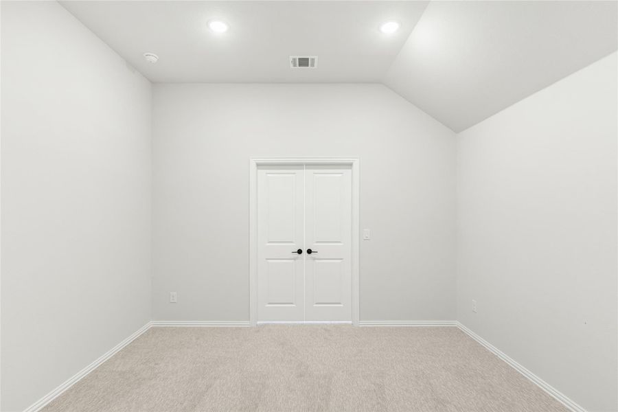Empty room with vaulted ceiling, carpet flooring, and white double doors with black handles