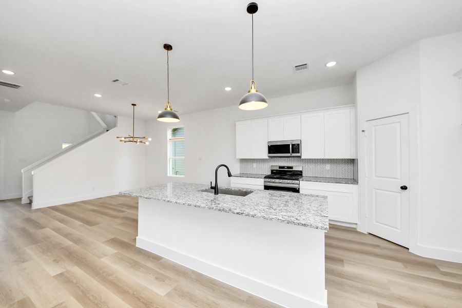 Spacious open-concept kitchen with large island, granite countertops, white cabinetry, and modern pendant lighting