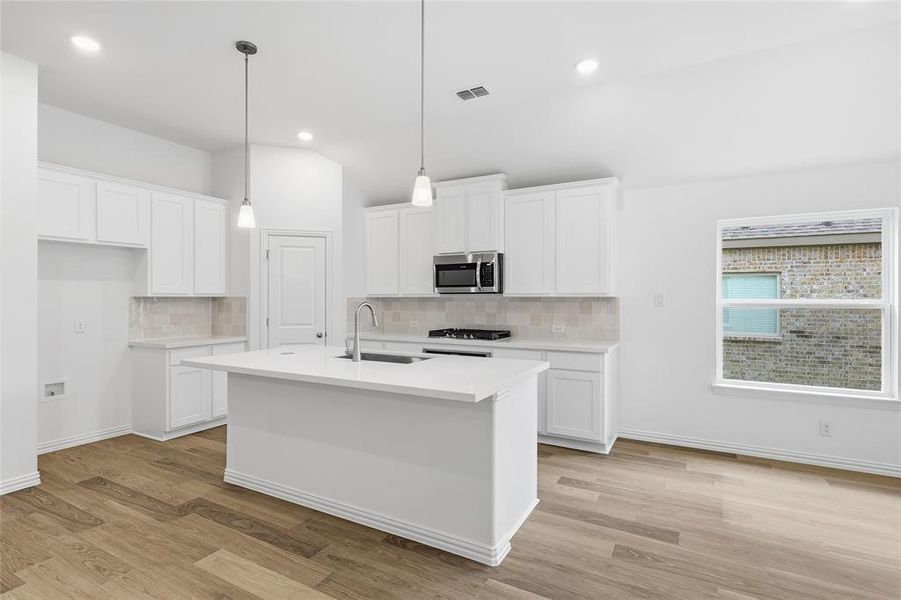 Bright kitchen featuring a central island with a sink, white cabinetry, light countertops, and wood-finish flooring