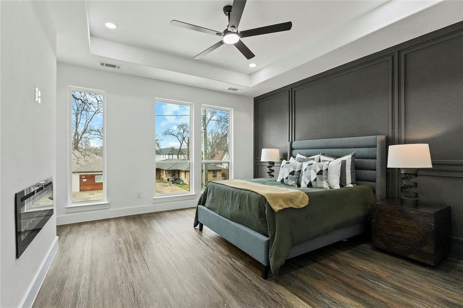 Bedroom with wood finished floors, a ceiling fan, recessed lighting, a tray ceiling, and a fireplace