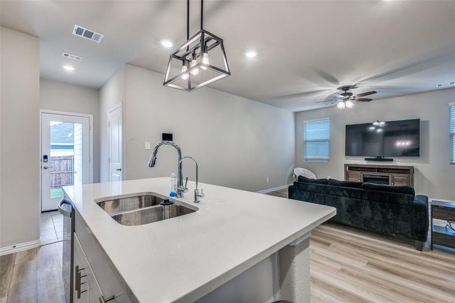 Kitchen with hanging light fixtures, light wood-style floors, a kitchen island with sink, recessed lighting, and open floor plan