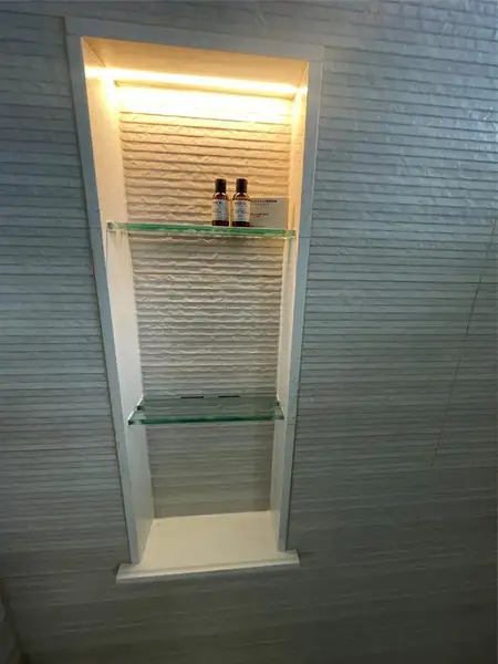 Recessed wall niche featuring integrated lighting, glass shelving, and textured wall finish