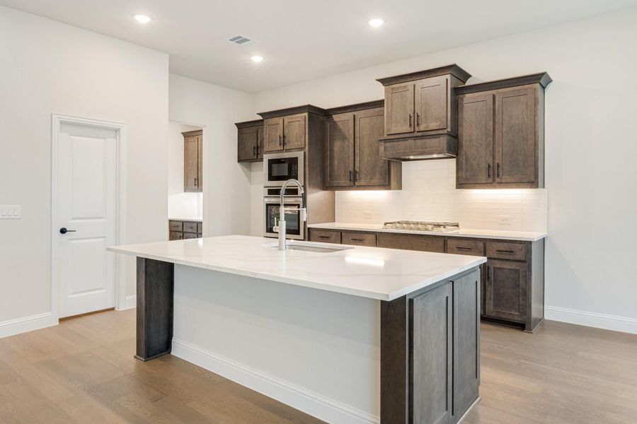 Kitchen with large white island, dark wood cabinets, stainless steel appliances, and light hardwood floors Kitchen with large white island, dark wood cabinets, stainless steel appliances, and light hardwood floors