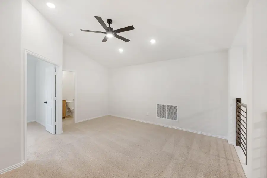 Empty bedroom with vaulted ceiling, ceiling fan, carpet flooring, and ensuite bathroom doorway