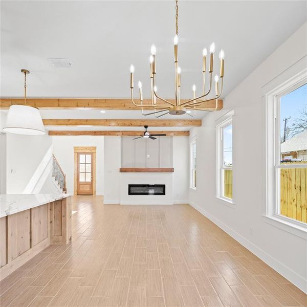 Unfurnished living room with a glass covered fireplace, a chandelier, ceiling fan, wood finish floors, and beamed ceiling Unfurnished living room with a glass covered fireplace, a chandelier, ceiling fan, wood finish floors, and beamed ceiling
