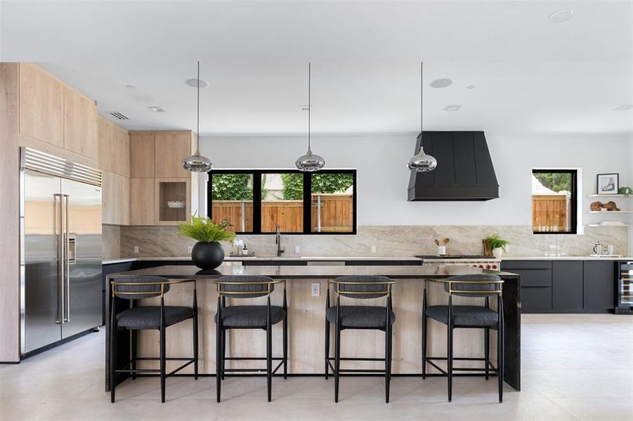 Kitchen with a wealth of natural light, stainless steel built in fridge, tasteful backsplash, and custom range hood