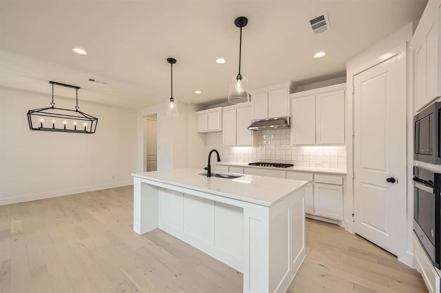 Kitchen with tasteful backsplash, light wood-style flooring, recessed lighting, an island with sink, and white cabinetry Kitchen with tasteful backsplash, light wood-style flooring, recessed lighting, an island with sink, and white cabinetry