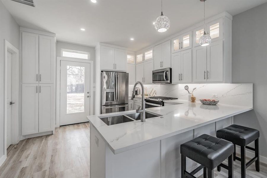 Kitchen featuring stainless steel appliances, decorative light fixtures, kitchen peninsula, and white cabinets