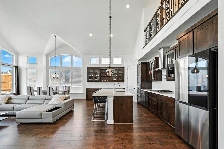 Kitchen with stainless steel appliances, wall chimney exhaust hood, dark brown cabinetry, high vaulted ceiling, and recessed lighting