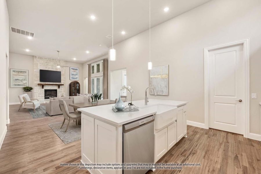 Open-concept kitchen with white island, farmhouse sink, and view of living room with stone fireplace Open-concept kitchen with white island, farmhouse sink, and view of living room with stone fireplace