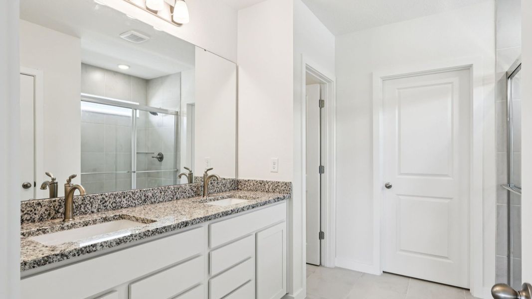 Primary Suite Bathroom with Granite Countertops, Dual Sinks, and White Cabinets in the Baker by DRB Homes Willowbrook North