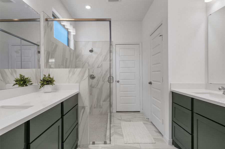 Bathroom featuring a marble finish shower, two vanities, and light marble finish floors