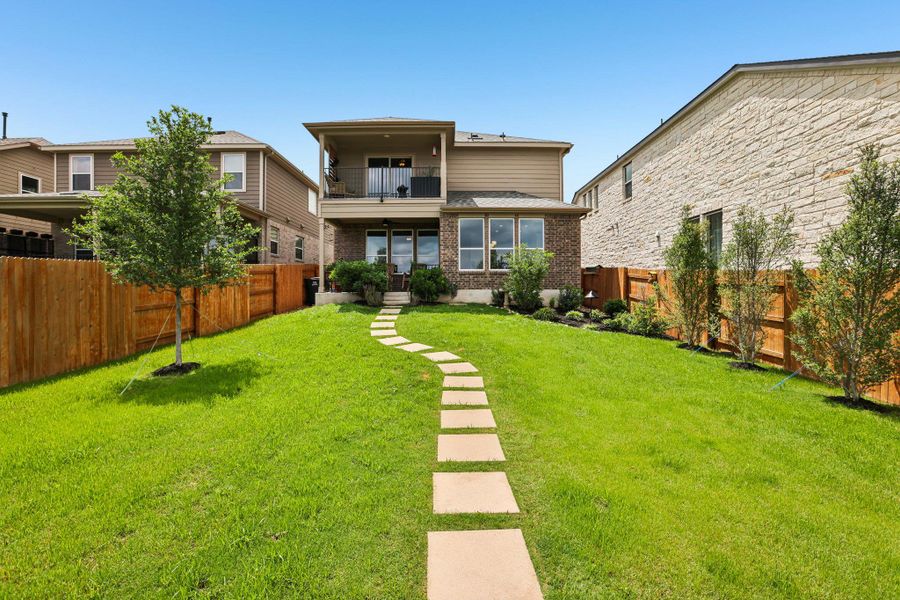 The property features a spacious backyard with a well-maintained lawn and a stone-paved pathway leading to the home's rear entrance