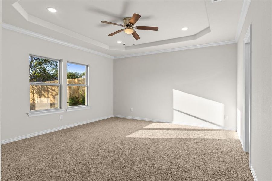 Empty room with a raised ceiling, carpet flooring, ceiling fan, crown molding, and recessed lighting