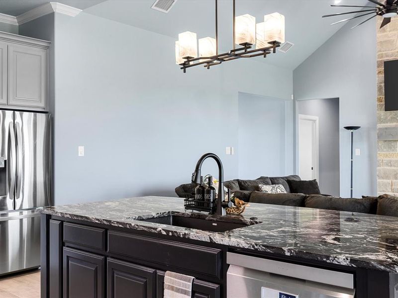 Kitchen with dark stone counters, stainless steel appliances, pendant lighting, open floor plan, and vaulted ceiling Kitchen with dark stone counters, stainless steel appliances, pendant lighting, open floor plan, and vaulted ceiling