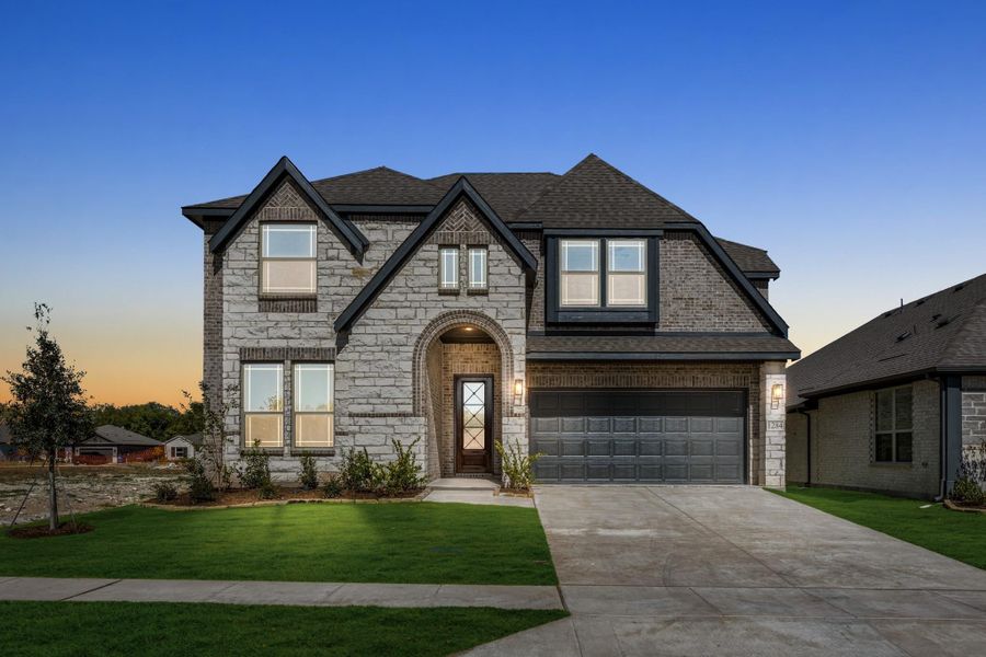 Two-story home with stone and brick exterior, arched entry, two-car garage, and green front lawn at dusk Two-story home with stone and brick exterior, arched entry, two-car garage, and green front lawn at dusk