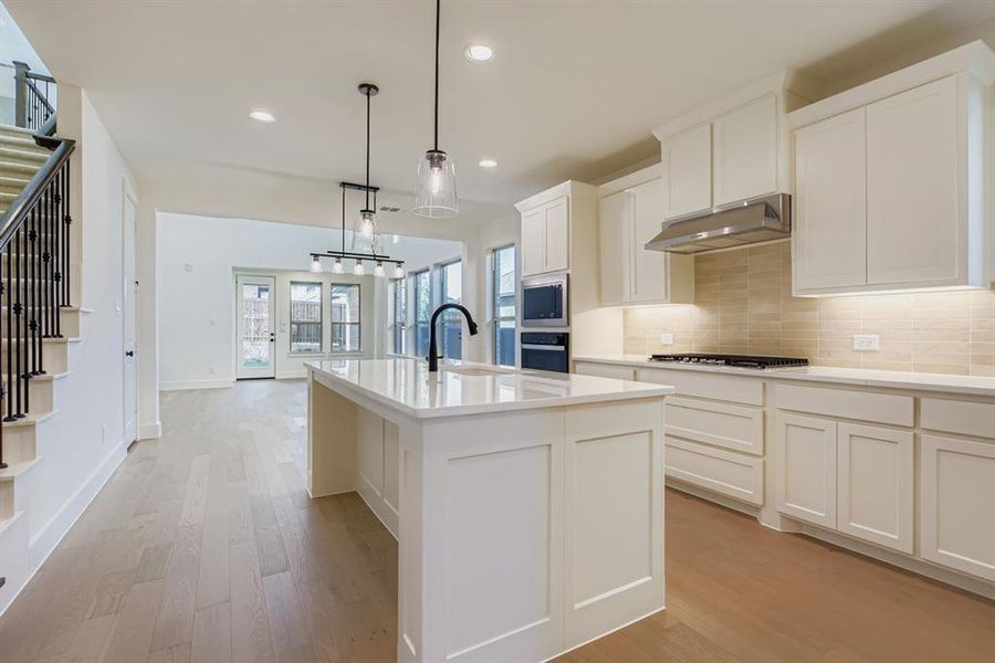 Kitchen featuring decorative backsplash, recessed lighting, an island with sink, decorative light fixtures, and white cabinets