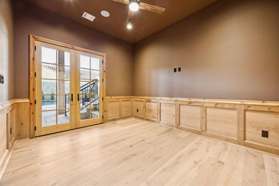 Spare room featuring french doors, wainscoting, light wood-style floors, ceiling fan, and a decorative wall