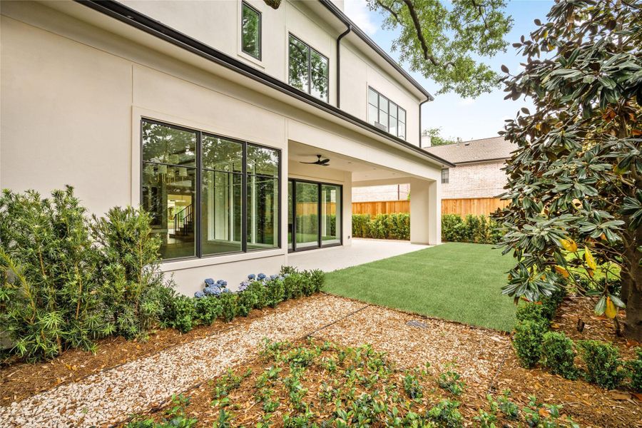 Alternate view of the backyard highlighting the home’s rear elevation, expansive windows, and covered patio.