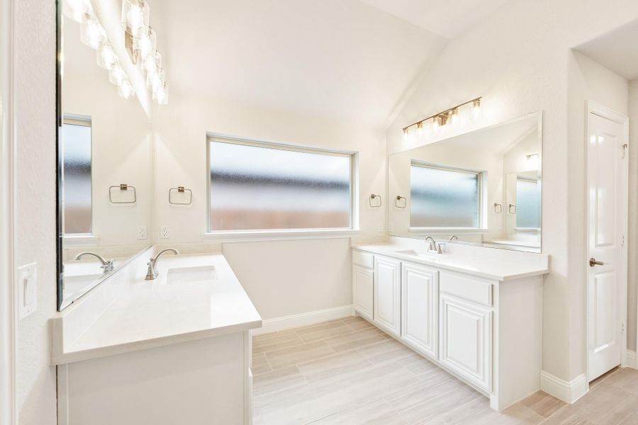 Bathroom with dual vanities, white cabinets, large mirrors, and light wood-style floors