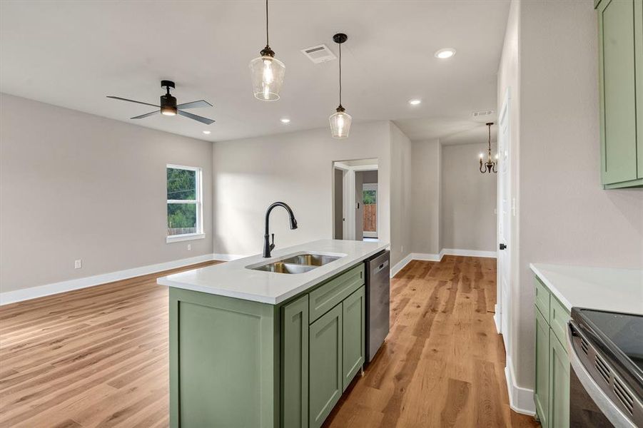 Kitchen featuring green cabinetry, recessed lighting, an island with sink, pendant lighting, and light wood-style flooring