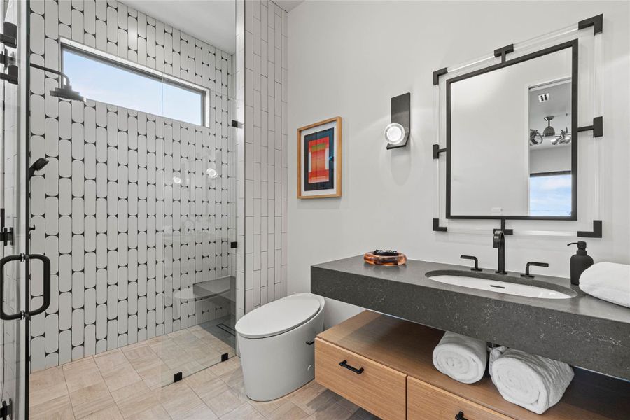 Contemporary bathroom featuring a spacious glass-enclosed shower with black-tiled walls, a built-in shower bench, a fixed showerhead, and a handheld sprayer