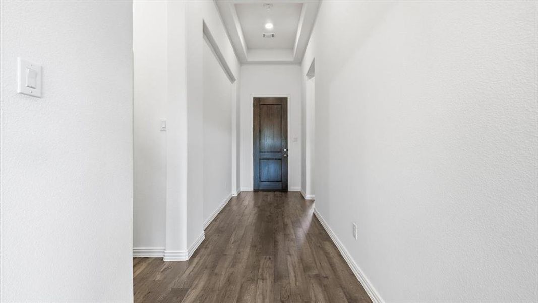 Hallway featuring wood-finish flooring, white baseboards, recessed lighting, and a dark wood door