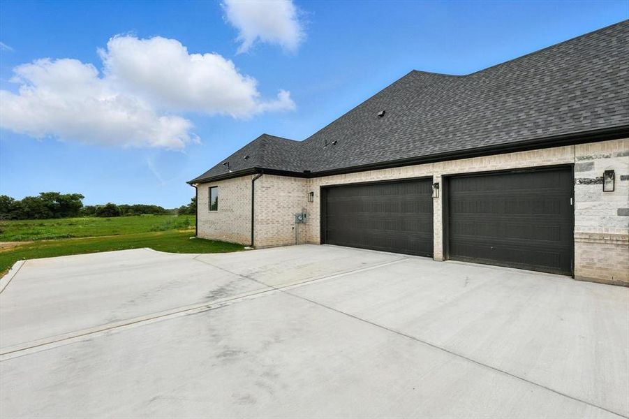 View of side of home with driveway, a garage, a shingled roof, brick siding, and a lawn View of side of home with driveway, a garage, a shingled roof, brick siding, and a lawn