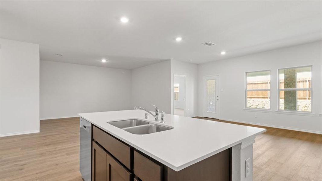 Kitchen with open floor plan, light wood-style floors, a kitchen island with sink, recessed lighting, and dark wood finish cabinets