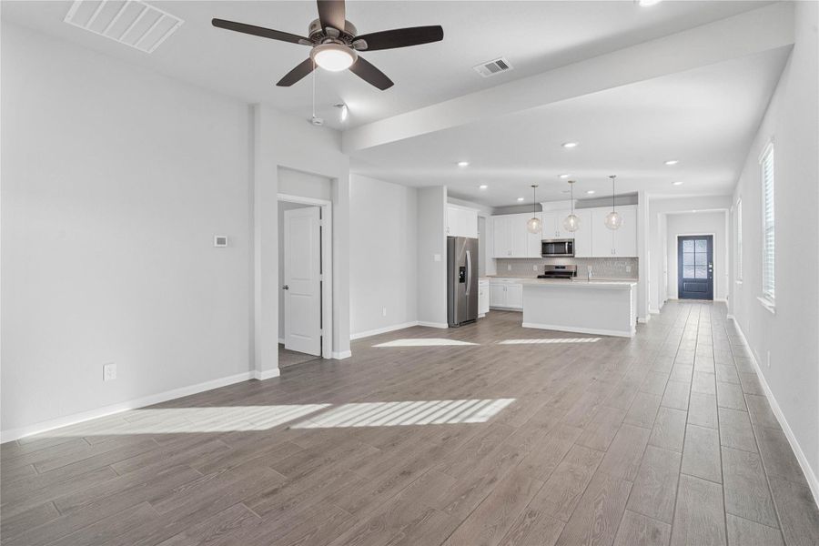 This expansive view from the back of the house showcases a seamless, open-concept layout that creates a warm and inviting path for guests, drawing the eye past the heart of the home toward the welcoming front entryway.