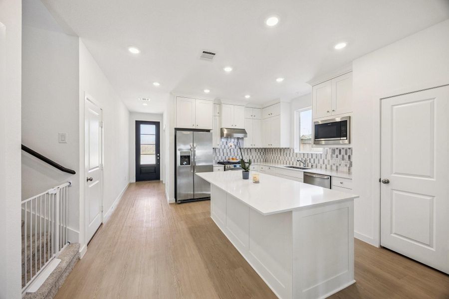 The modern style kitchen has floor to ceiling white cabinets and an extended island quartz countertop. Great countertop space for easily prepping food and enjoying family and friends get togethers.