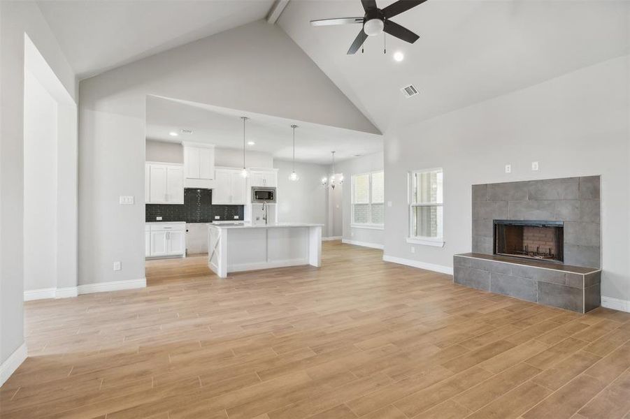 Unfurnished living room featuring light hardwood / wood-style floors, a tiled fireplace, beam ceiling, high vaulted ceiling, and ceiling fan