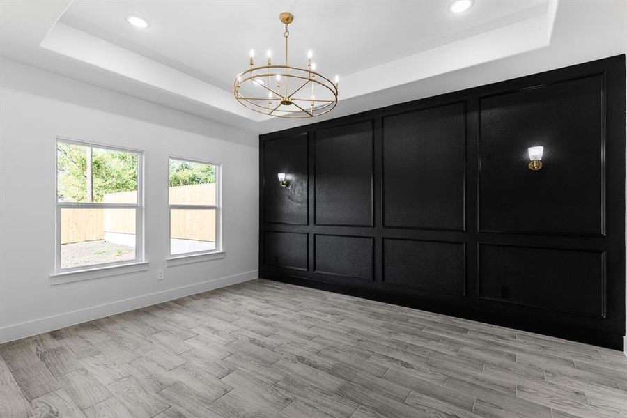 Spare room featuring a tray ceiling, a notable chandelier, and light hardwood / wood-style floors