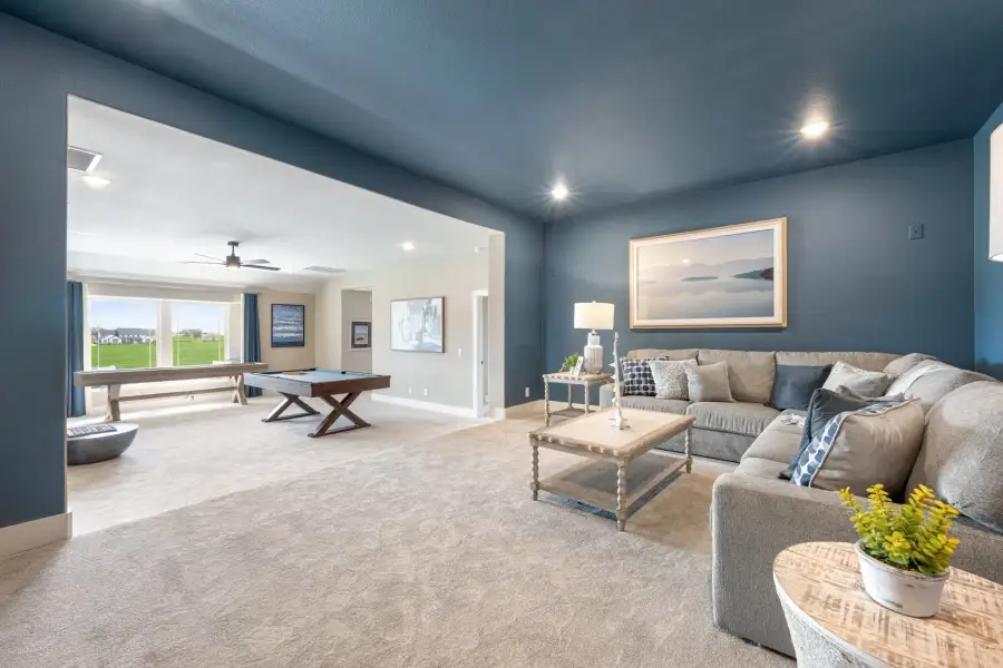 Open-concept living area with blue walls, sectional sofa, and adjoining game room with pool table and shuffleboard Open-concept living area with blue walls, sectional sofa, and adjoining game room with pool table and shuffleboard