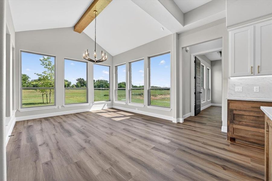 Vaulted ceiling great room featuring wood-finish flooring, a contemporary chandelier, exposed wood beam, and multiple large windows