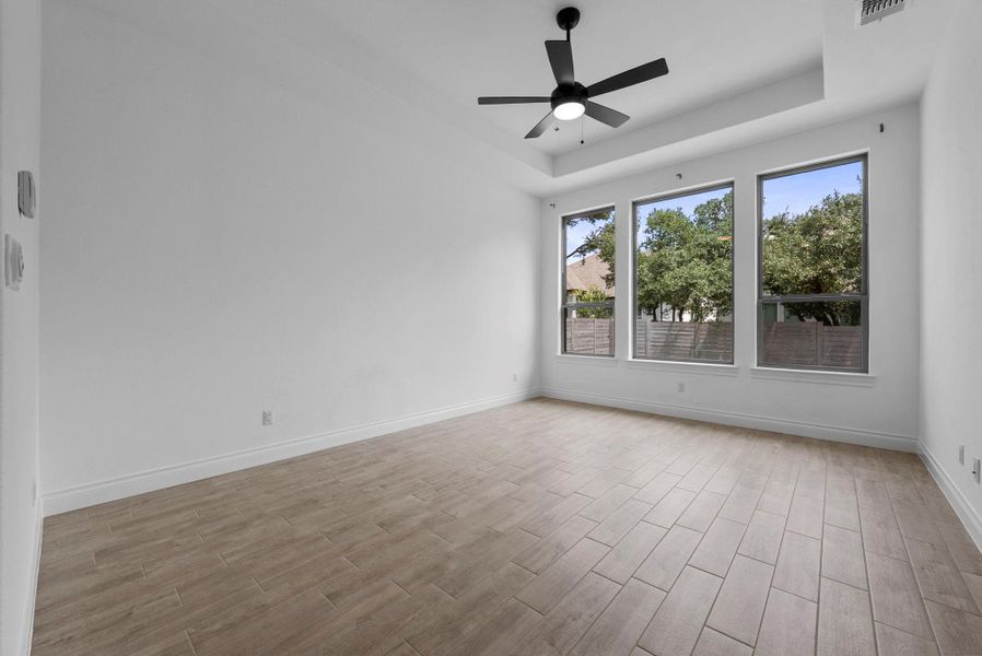 Spacious bedroom with wood-look flooring, tray ceiling, and large windows for abundant natural light.