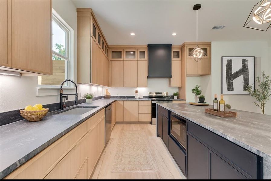 Kitchen with light brown cabinetry, appliances with stainless steel finishes, recessed lighting, extractor fan, and glass insert cabinets