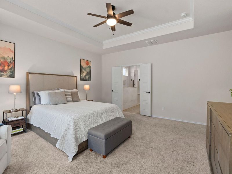 Bedroom with light carpet, ensuite bath, a ceiling fan, and a tray ceiling