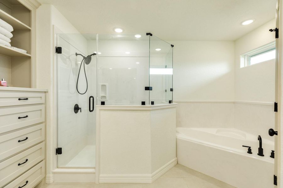 This bathroom features a modern glass-enclosed shower, a spacious bathtub, and built-in shelving with ample storage. The design is bright and clean, with neutral tones and recessed lighting.