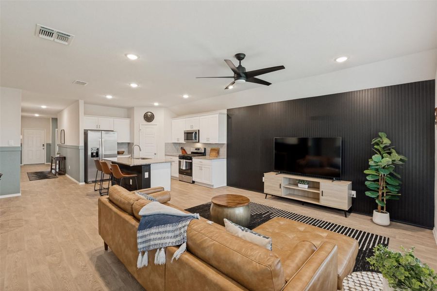An open concept living area seamlessly flows into the kitchen, featuring light wood flooring and modern recessed lighting.