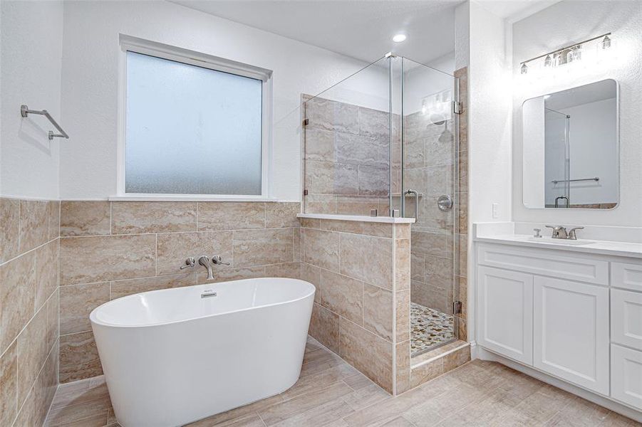 Full bathroom featuring tile walls, a shower stall, a freestanding bath, vanity, and a wainscoted wall Full bathroom featuring tile walls, a shower stall, a freestanding bath, vanity, and a wainscoted wall