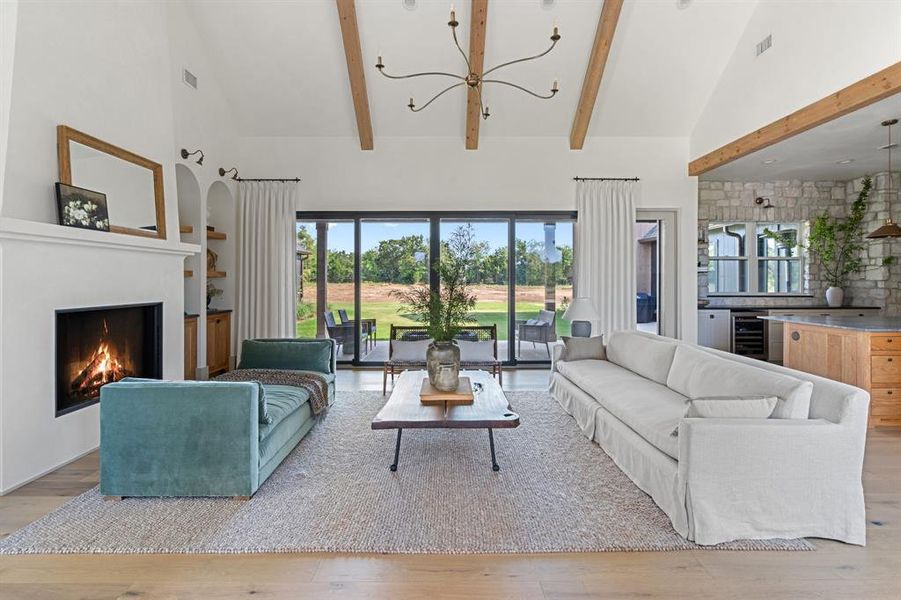 Living room with light hardwood / wood-style floors, beverage cooler, beam ceiling, high vaulted ceiling, and a chandelier